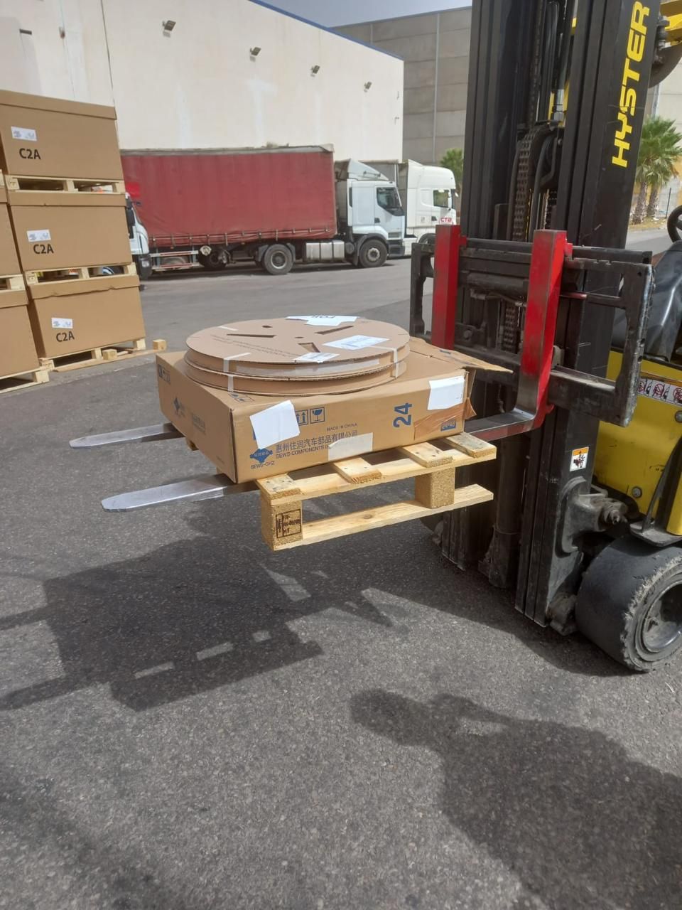A forklift lifting a pallet loaded with a reel and a carton on a company yard.